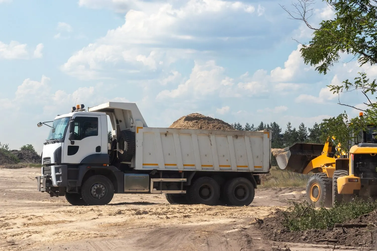 White dump truck loaded with sand beside a wheel loader at a construction site
