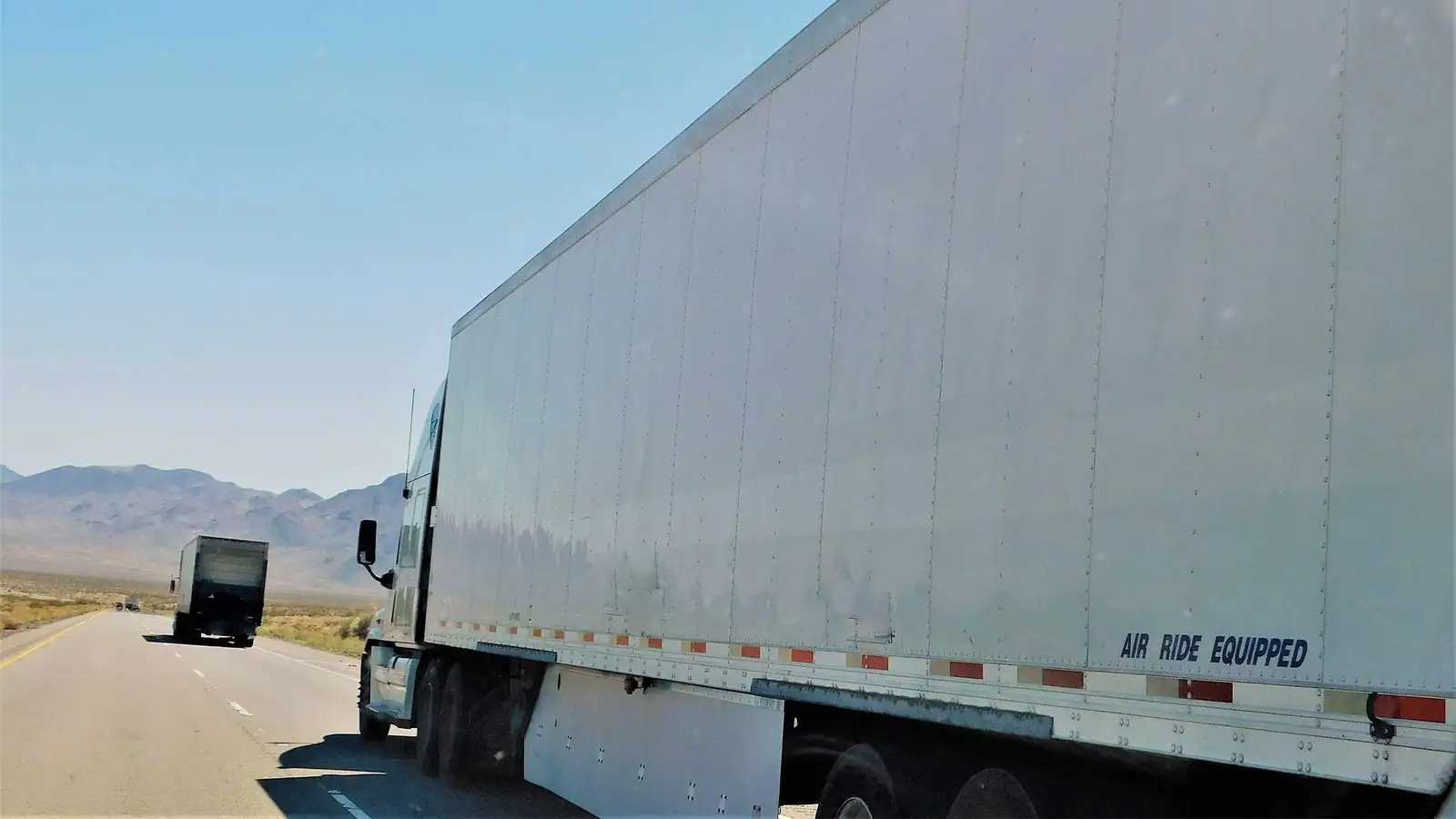 White dry van semi-trailer running an open interstate between mountain ranges