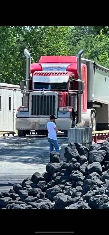 Worker standing beside a red dump truck loading at a rock yard