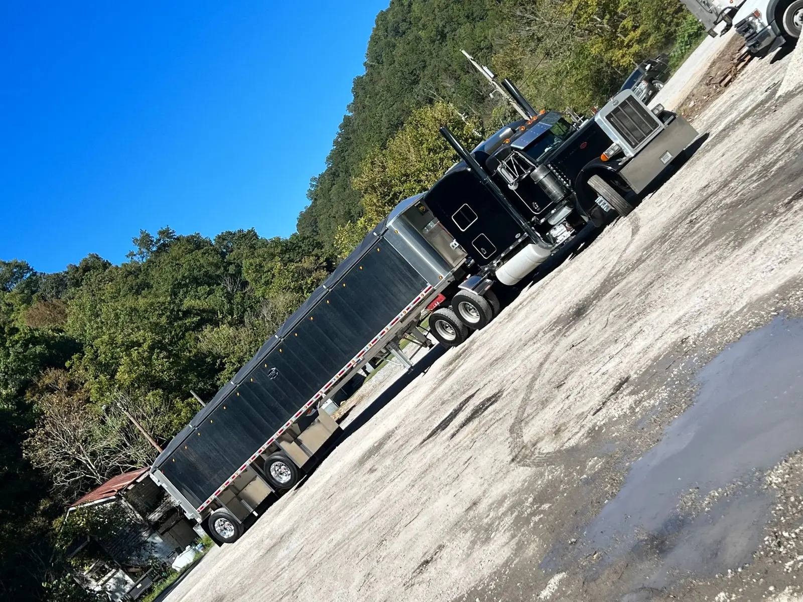 Black Mullins Trucking Peterbilt hooked to an aluminum end-dump trailer on gravel