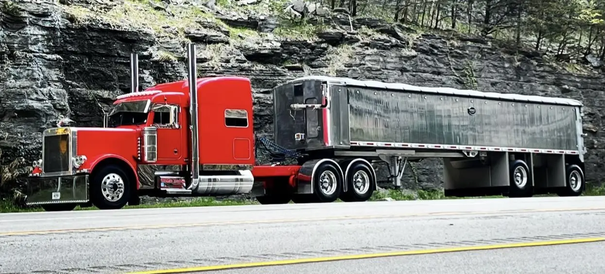 Red Mullins Trucking Peterbilt hauling an aluminum grain trailer past a Kentucky rock cut