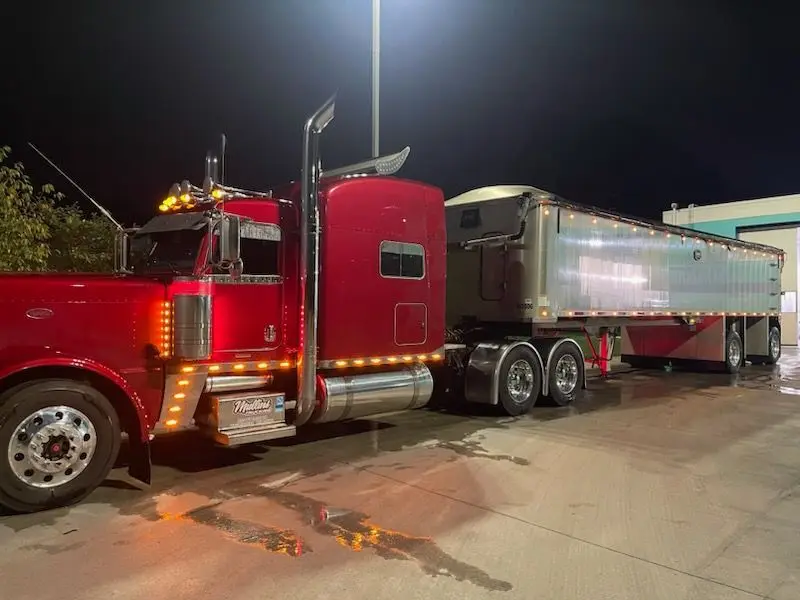 Red Mullins Trucking Peterbilt and lit aluminum dump trailer parked at night