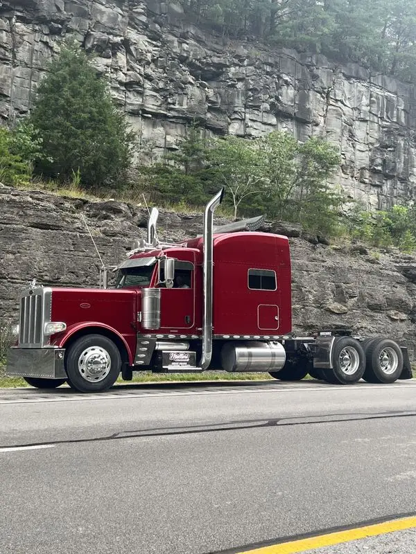 Maroon Mullins Trucking Peterbilt bobtail on a Kentucky highway shoulder below a rock cut