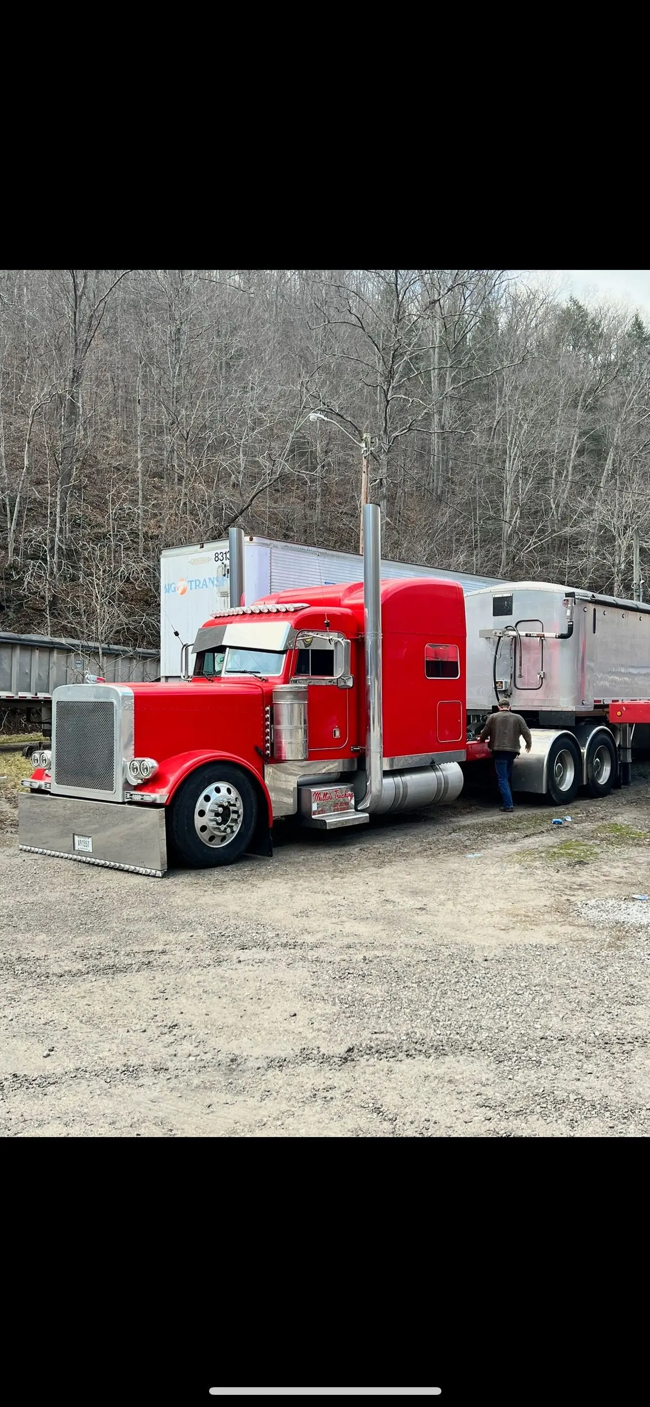 Red Mullins Trucking Peterbilt and trailer parked at the yard with a driver alongside