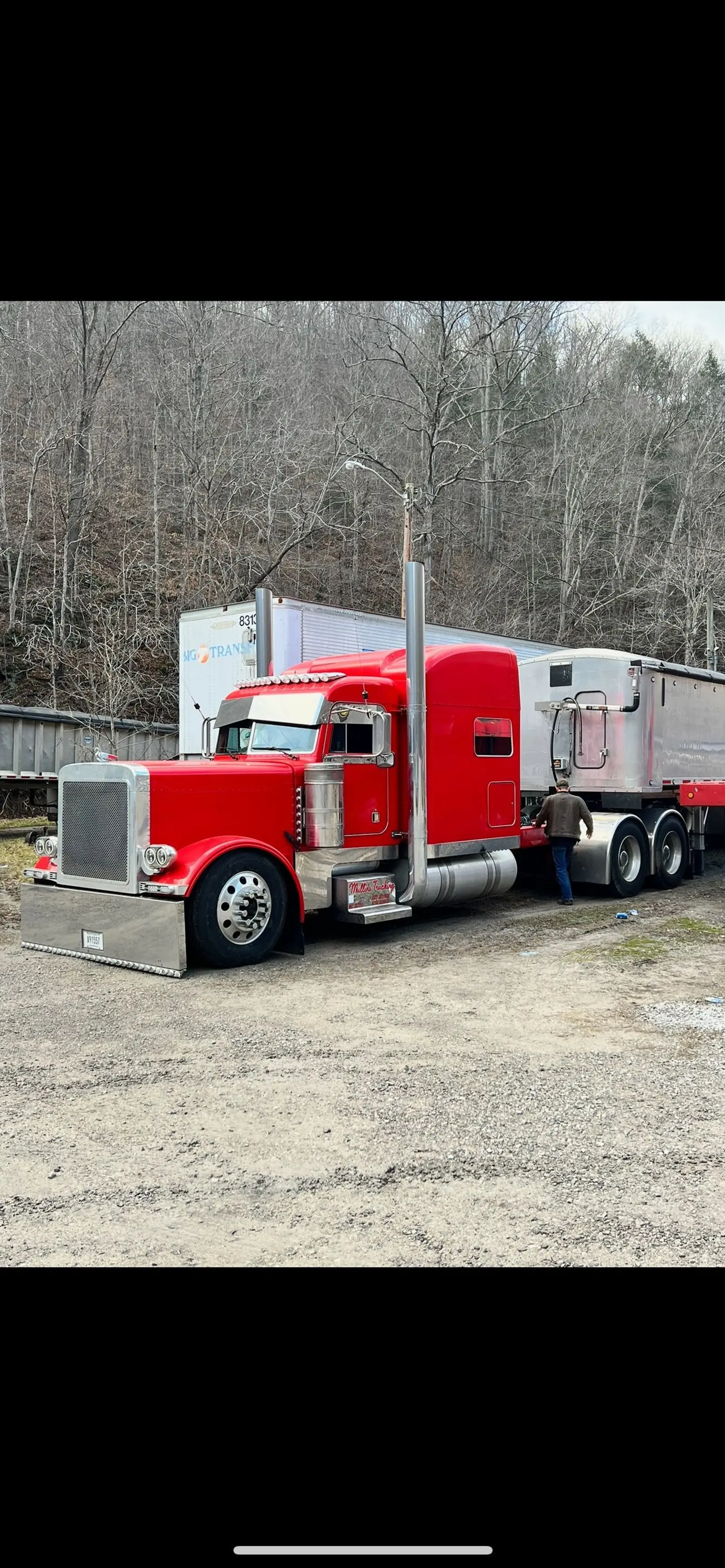 Red Mullins Trucking Peterbilt and trailer parked at the yard with a driver alongside
