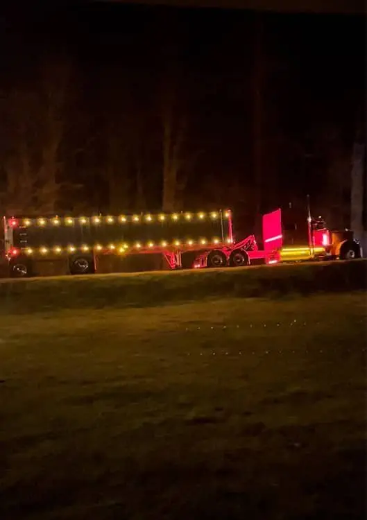 Mullins Trucking tractor and step-deck trailer outlined in marker lights at night