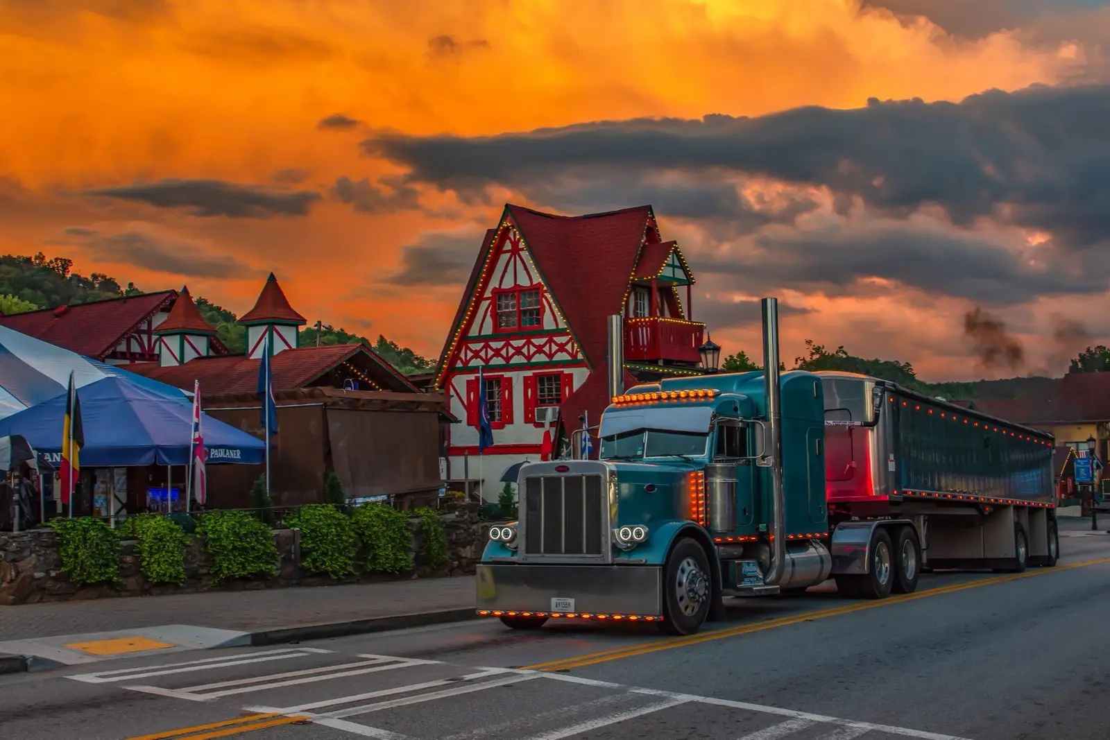 Teal Peterbilt pulling a grain trailer down a village main street at sunset